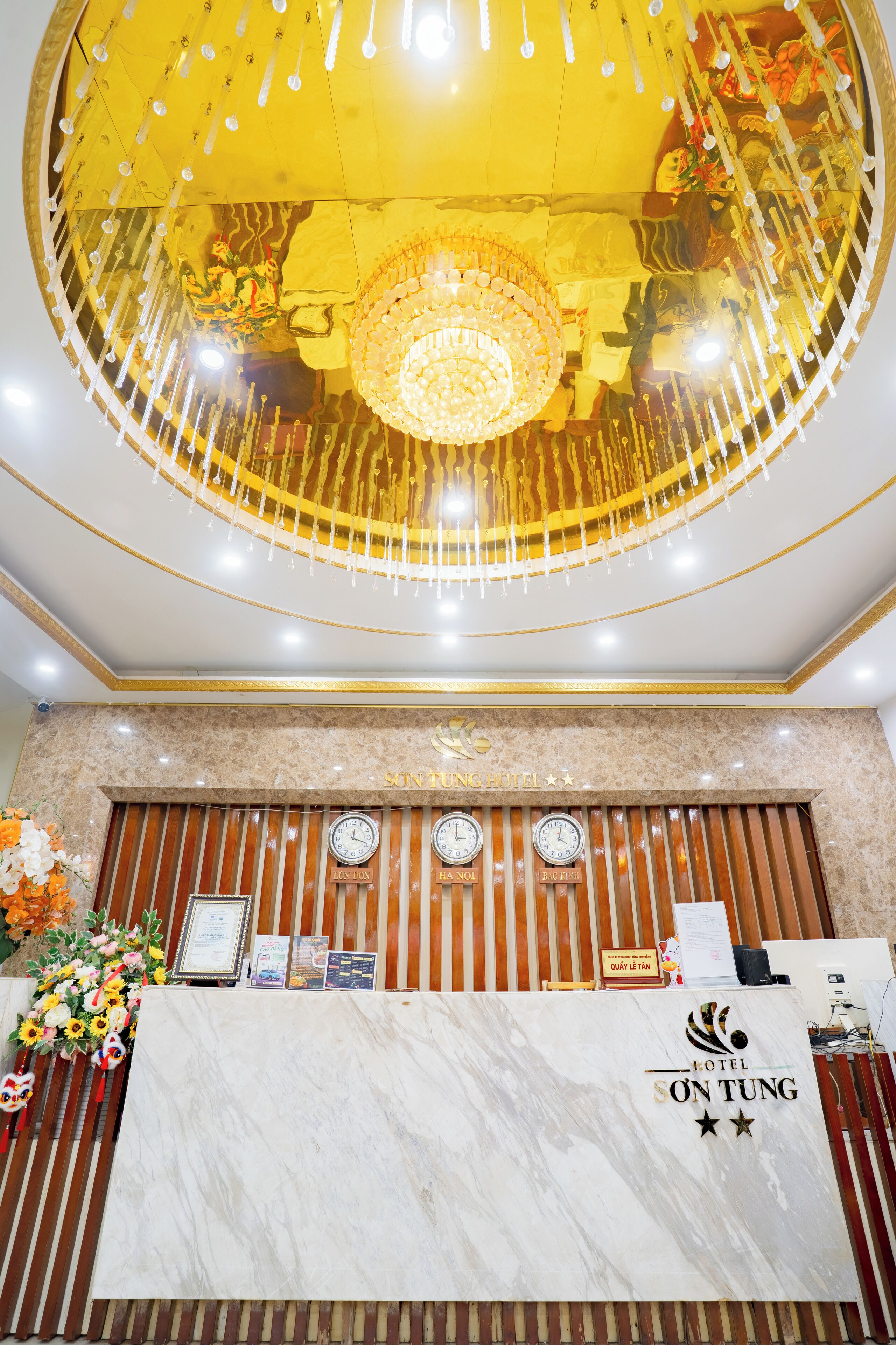 A hotel reception desk with a marble top, a chandelier, and clocks indicating different time zones.