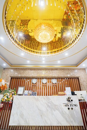 A hotel reception desk with a marble top, a chandelier, and clocks indicating different time zones.