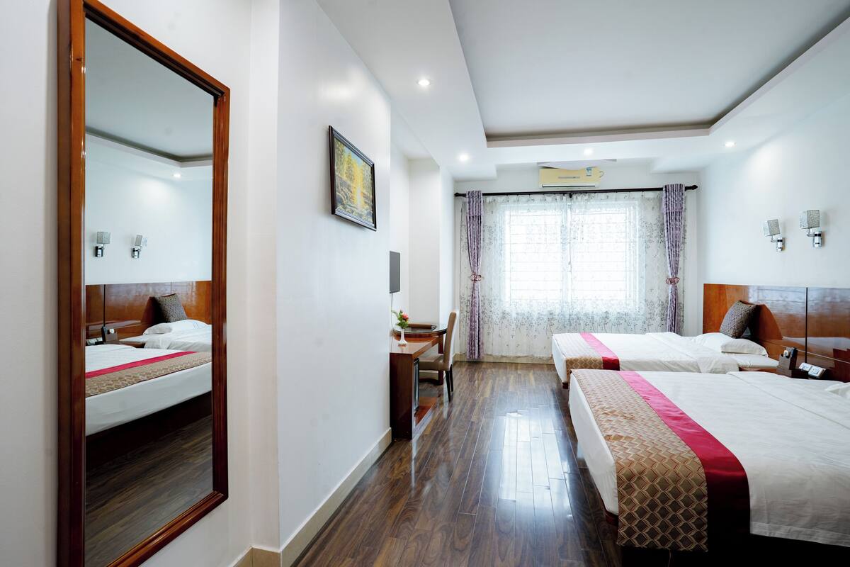 A hotel room with two beds, a desk, and a large mirror.