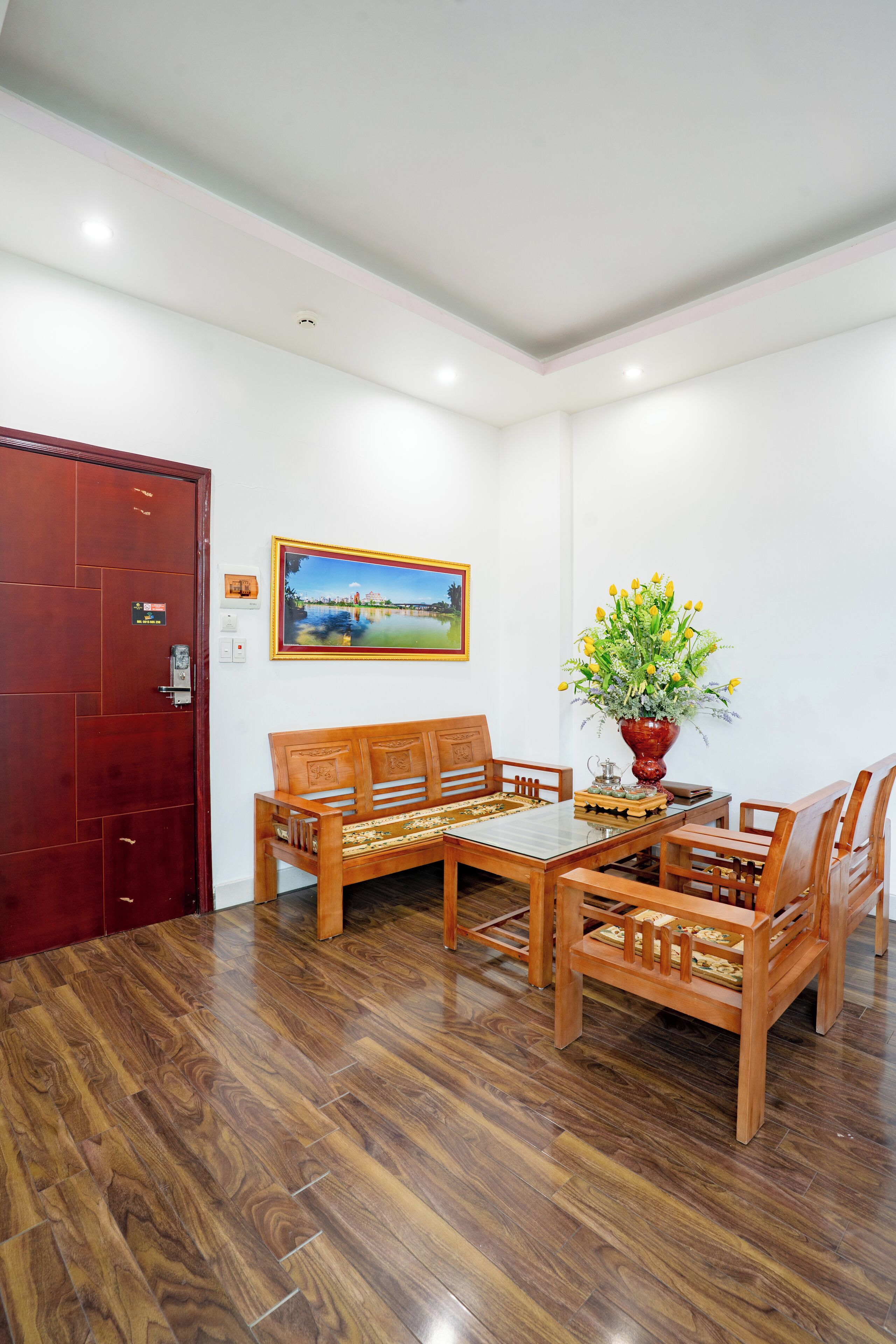 Una habitación con una mesa y sillas de madera, una puerta roja, un cuadro en la pared y un florero con flores.