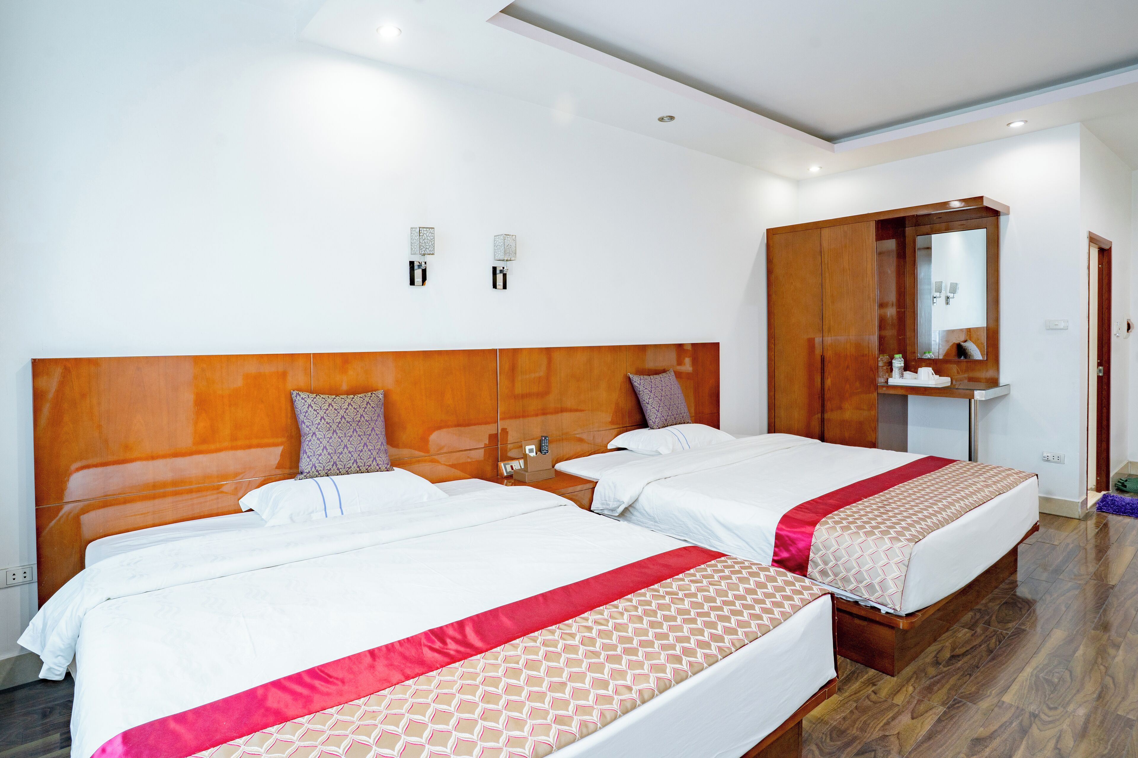 A hotel room with two beds, a wooden headboard, a mirror, and a small bathroom area.