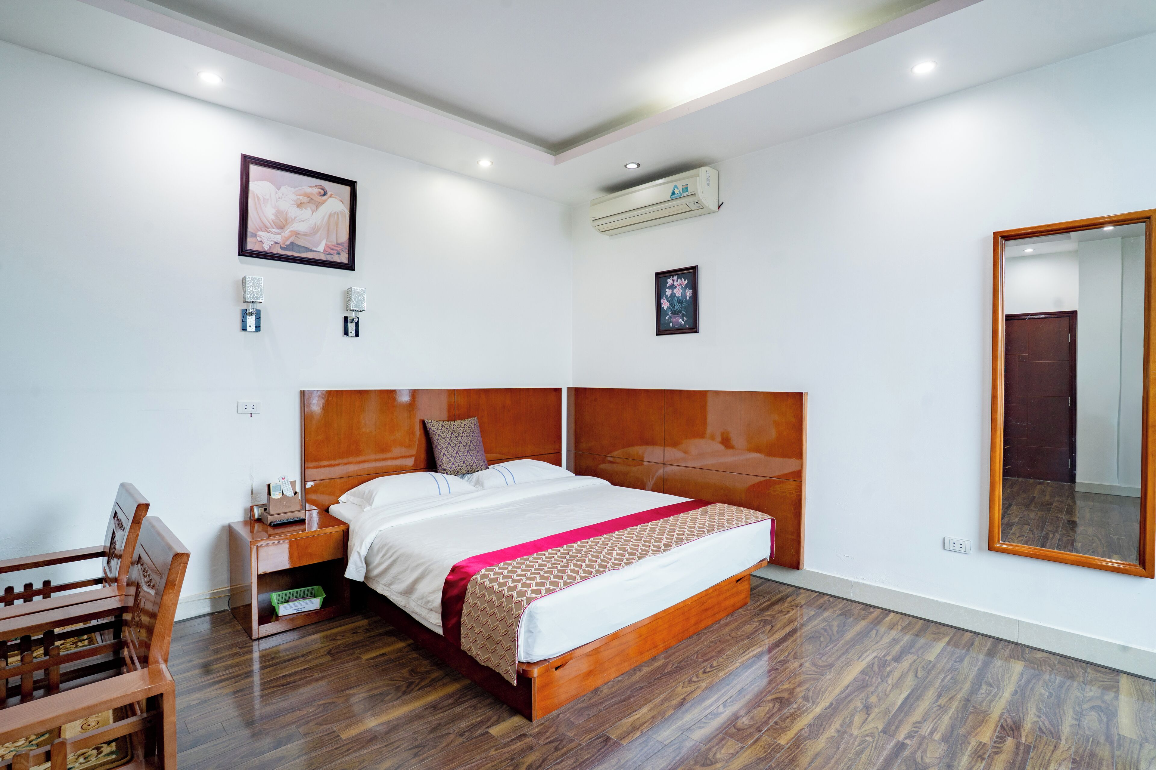 Quarto com cabeceira de madeira, uma cama grande, mesa de cabeceira, espelho e um banco de madeira.