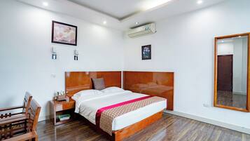 Quarto com cabeceira de madeira, uma cama grande, mesa de cabeceira, espelho e um banco de madeira.