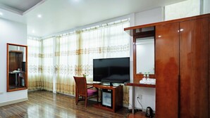A living room with a wooden floor, a TV on a wooden stand, a chair, a cabinet, and a window with curtains. - Son Tung Hotel - Kim Dong Walking Street (Thuc Phan)