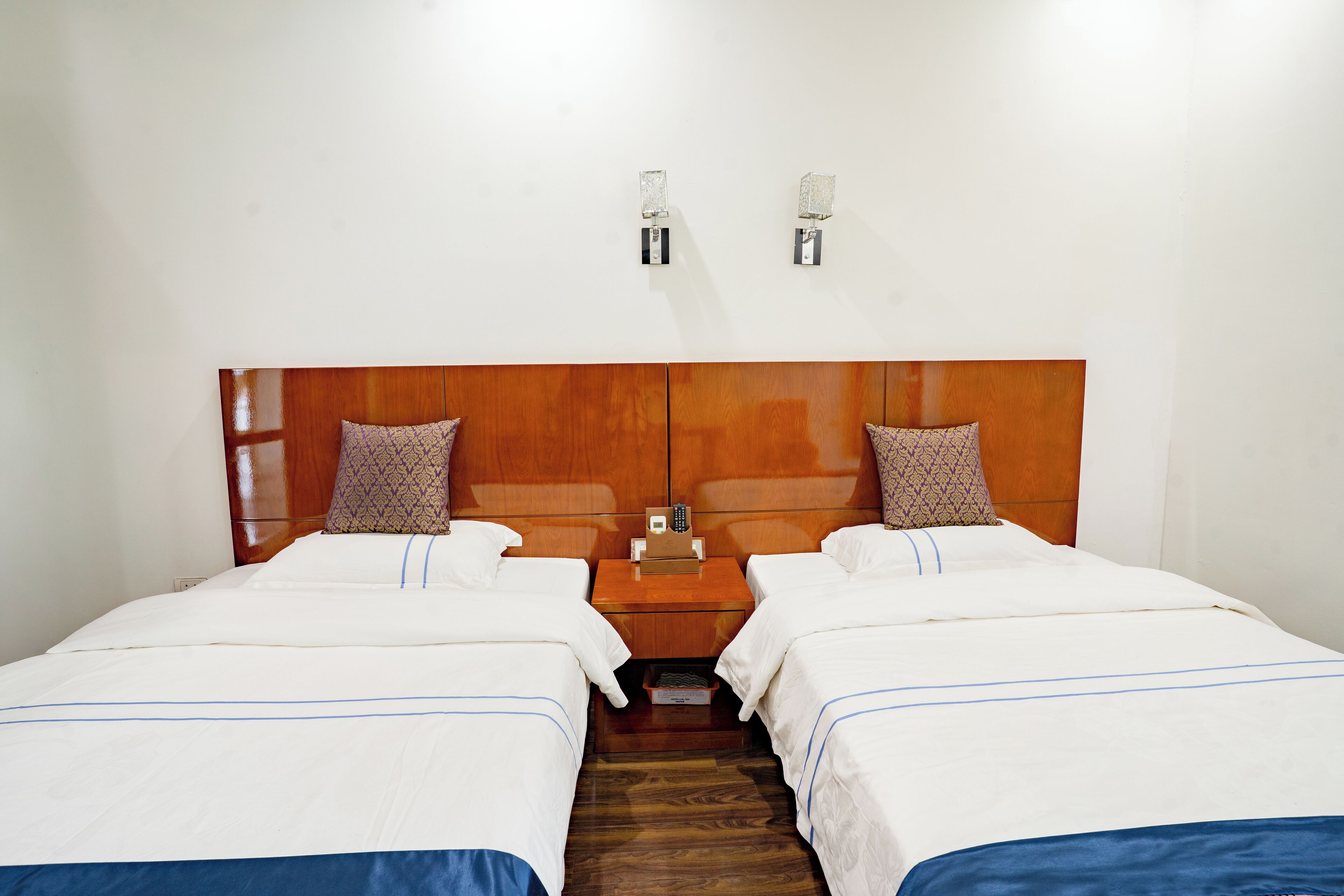 Ein Hotelzimmer mit zwei Betten, einem Holzkopfstück, Nachttischlampen und einem Nachttisch mit Telefon.