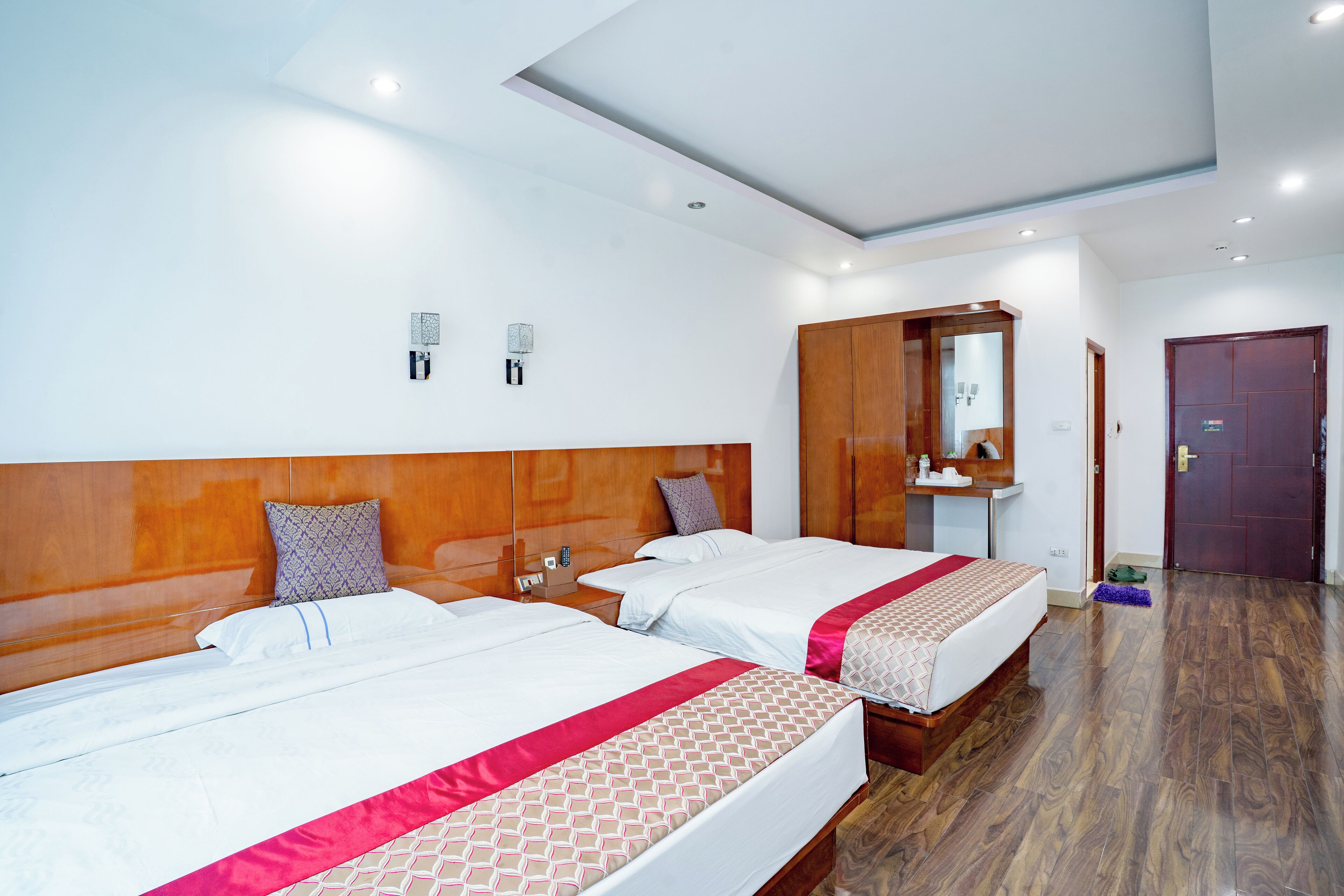 A hotel room with two beds, wooden headboards, white walls, and a wooden floor.