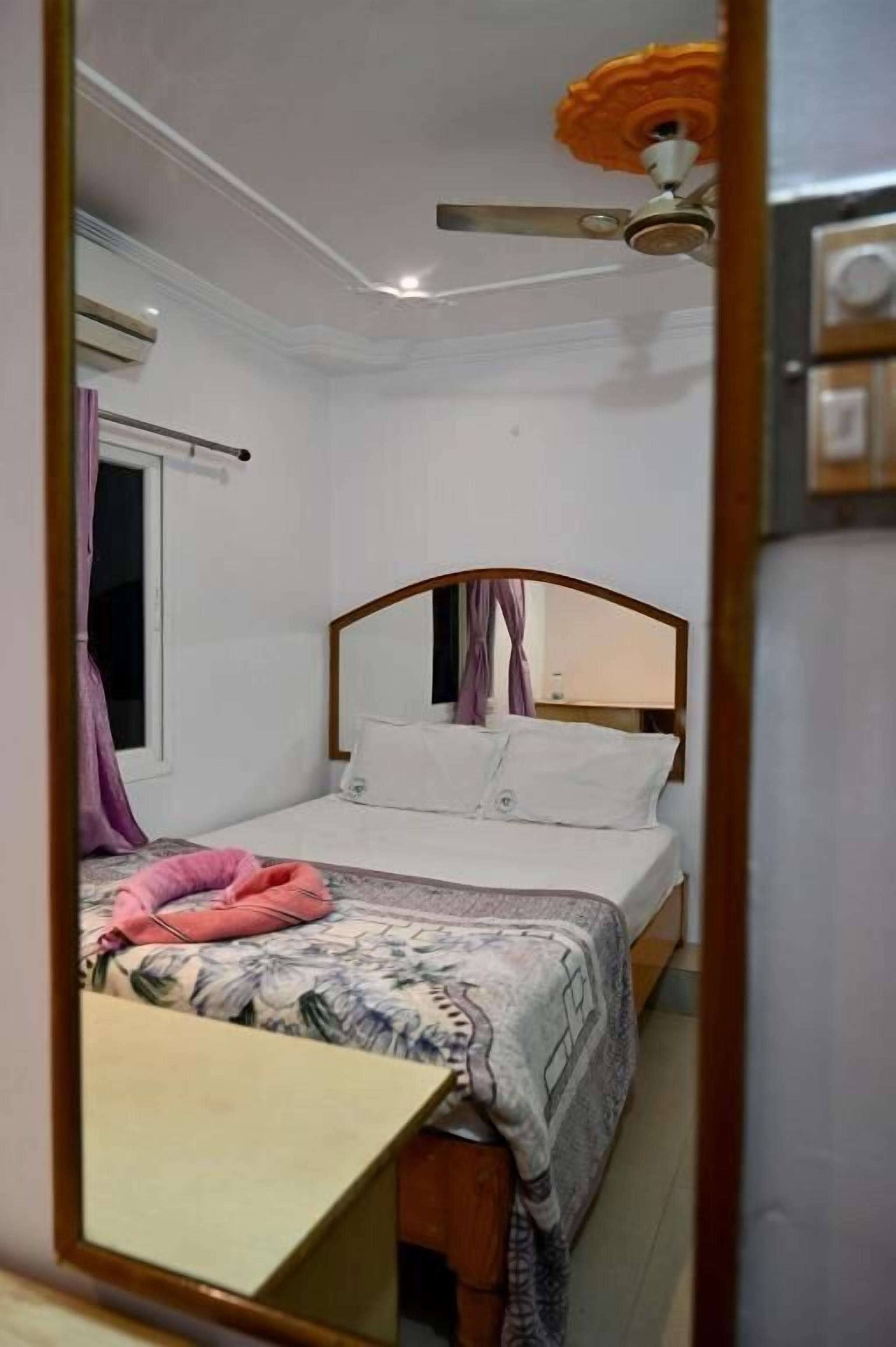 A bedroom with a bed, a ceiling fan, a window with curtains, and a mirror.