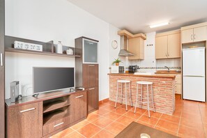 A modern kitchen with a TV, wooden cabinets, a brick island, and a refrigerator.