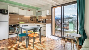 A modern kitchen with a dining area, large windows, and a view of the outdoors. - Le Crozet, quality cottage with panoramic mountain views (Plateau-des-Petites-Roches)