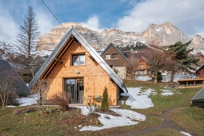 A wooden cabin with a sloped roof, a small porch, and a mountain backdrop. - Le Crozet, quality cottage with panoramic mountain views (Plateau-des-Petites-Roches)