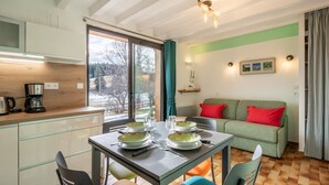 A modern kitchen with a dining area, a green sofa with red cushions, and a large window. - Le Crozet, quality cottage with panoramic mountain views (Plateau-des-Petites-Roches)