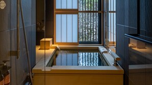 Une salle de bain moderne avec une baignoire sur pieds, une fenêtre équipée de stores verticaux et un tuyau de douche apparent.