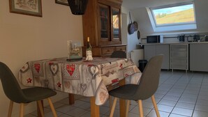 Een eetgedeelte met een tafel gedekt voor twee personen, een kast, een raam met uitzicht op een veld en een keuken met inbouwapparatuur.