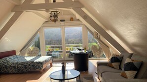 Ruime loft slaapkamer met groot raam, een bed, een bank en een kleine tafel.