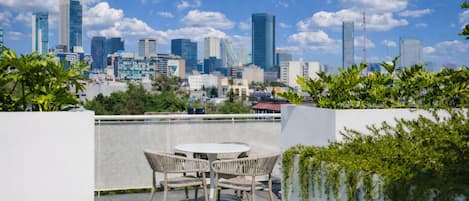 A rooftop terrace with a table and chairs, overlooking a city skyline with modern buildings.