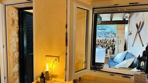 Un baño con un lavamanos amarillo, un espejo y una ventana que da a vista de herramientas de jardinería y una cama.