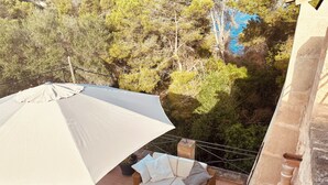 Un balcón con sombrilla blanca, mobiliario de mimbre y vistas a árboles y una masa de agua azul.