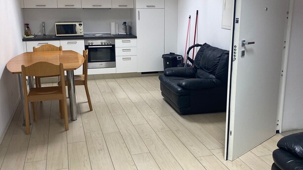 A compact living space with a kitchenette, a dining area with a wooden table and chairs, a black leather sofa, and a wooden coffee table. - Peaceful 2-bedroom apartment in charming Balerna perfect for relaxing stays (Balerna)