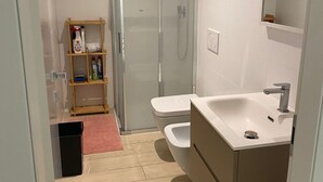 A modern bathroom with a glass-enclosed shower, a white sink, and a wooden shelf with toiletries. - Peaceful 2-bedroom apartment in charming Balerna perfect for relaxing stays (Balerna)