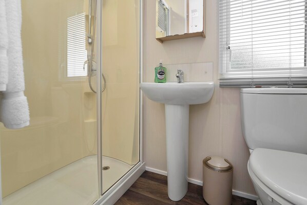 Une salle de bain avec une douche à parois de verre, un lavabo sur colonne et des toilettes.