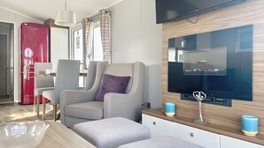 A modern living room with a sofa, ottoman, and a television mounted on a wooden wall. - Premium Lodge - Sleeps 8 - Seton Sands Beach (Prestonpans)