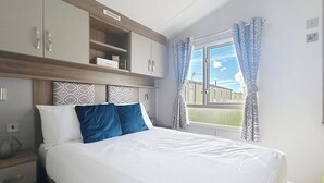 A hotel room with a bed, a nightstand, a wardrobe, and a window with curtains. - Premium Lodge - Sleeps 8 - Seton Sands Beach (Prestonpans)