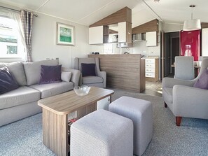 Un salon moderne comprenant un canapé, des fauteuils, une table basse et un coin cuisine avec des placards et un appareil électroménager rouge.