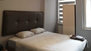 Une chambre avec un grand lit, un luminaire au plafond et une fenêtre équipée de stores.