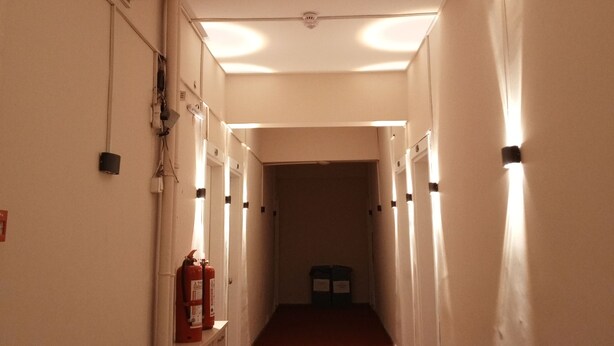 Un couloir étroit, doté d’une moquette rouge, de murs blancs et de plusieurs luminaires disposés le long du plafond.