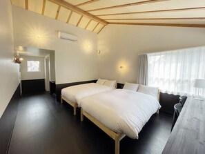 A hotel room with a large bed, a desk with a chair, a window with curtains, and an air conditioning unit. - Lapis Jogasaki B&B (Ito)