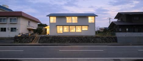 Una casa moderna de dos pisos con un muro de piedra en el frente y una escalera que lleva a la entrada, bajo un cielo despejado.