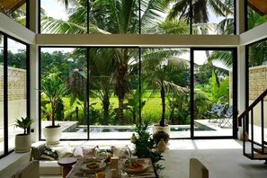 Zona pranzo moderna con vista su un rigoglioso giardino e palme attraverso ampie finestre.