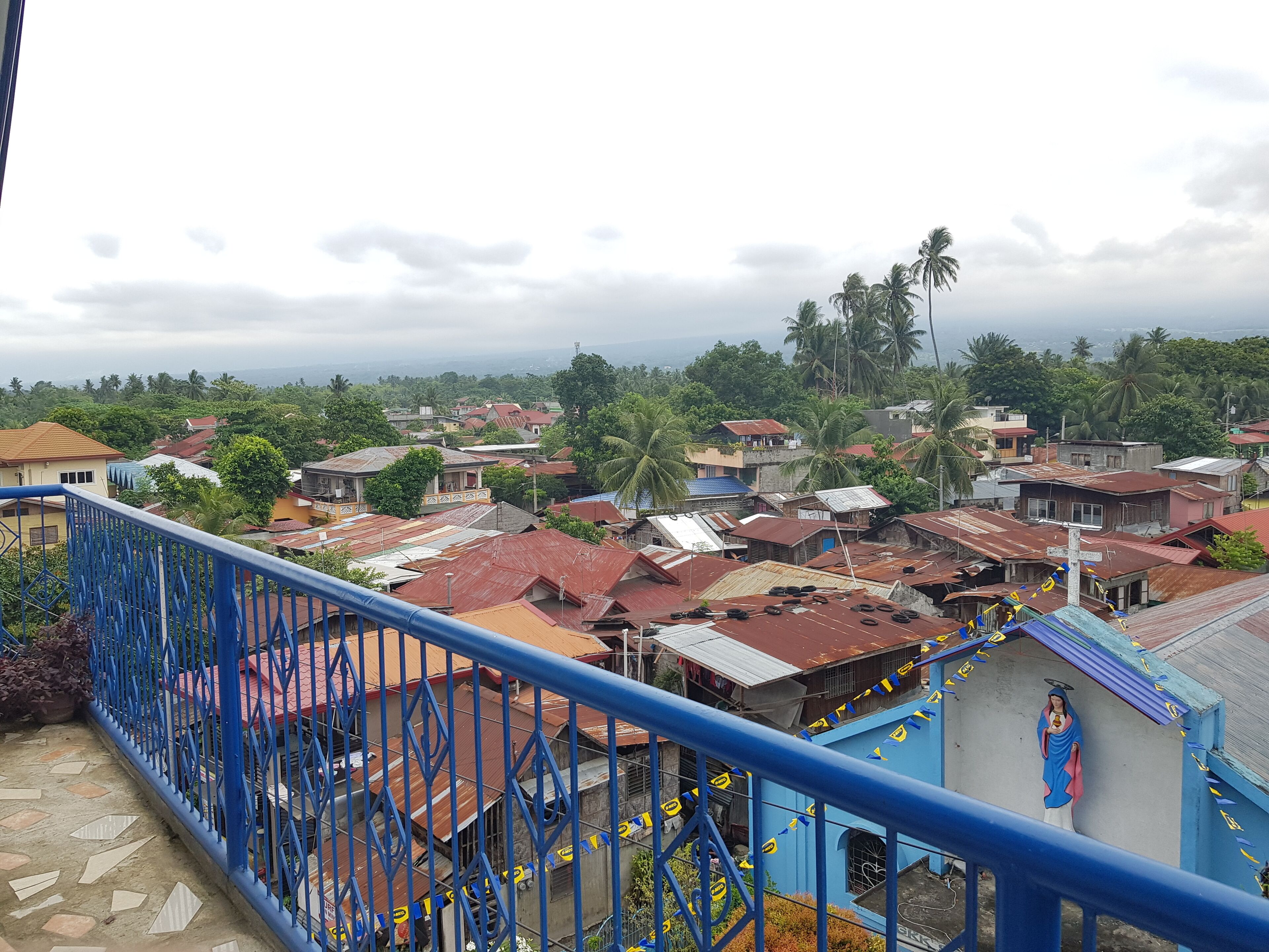 Un barrio residencial con casas, algunas con techos de hojalata, y un edificio azul con una cruz.