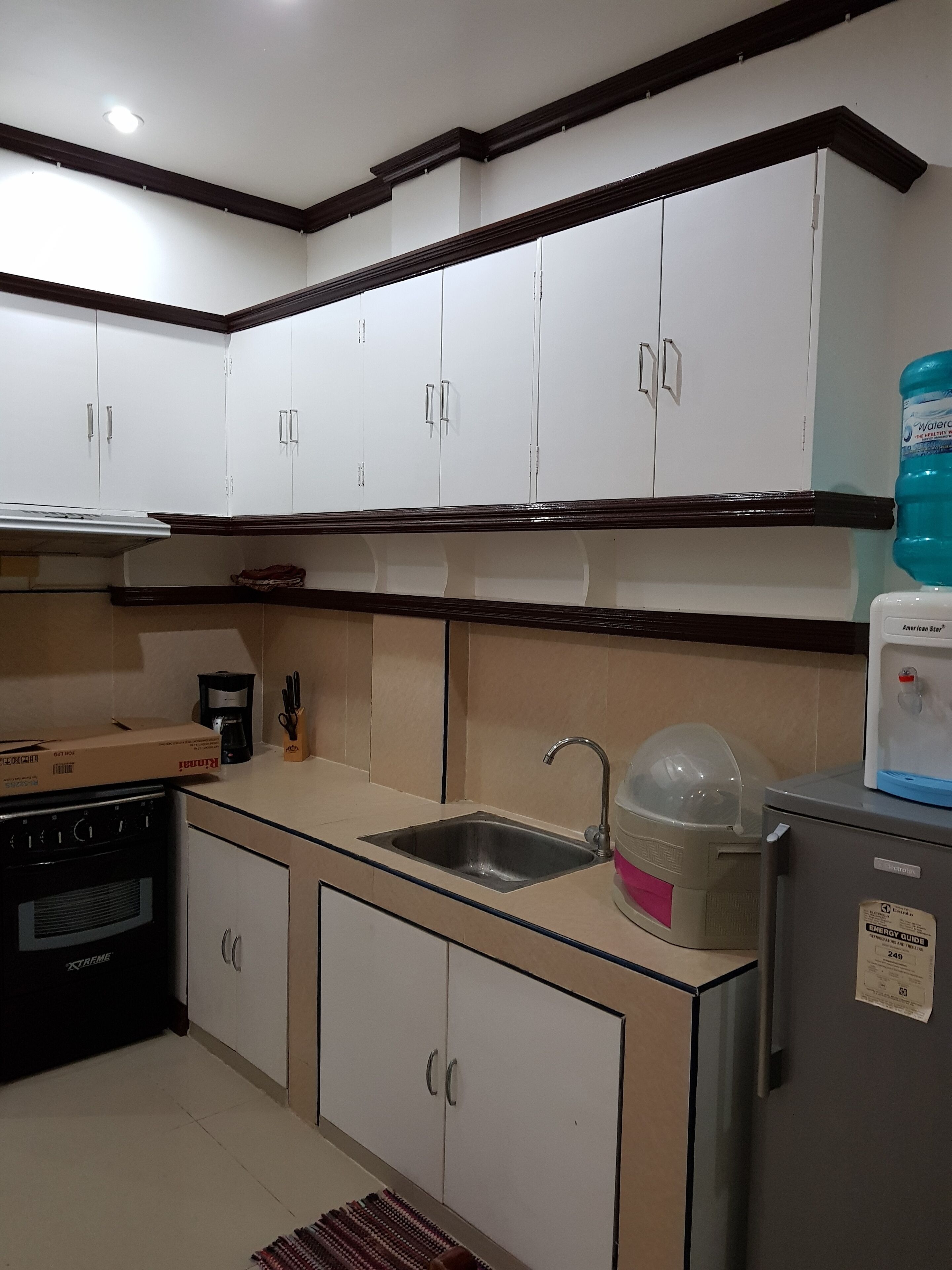 A kitchen with white cabinets, a stainless steel sink, a refrigerator, and a water dispenser.