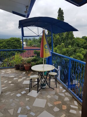 A covered outdoor seating area with a table and chairs, surrounded by blue railings and potted plants.