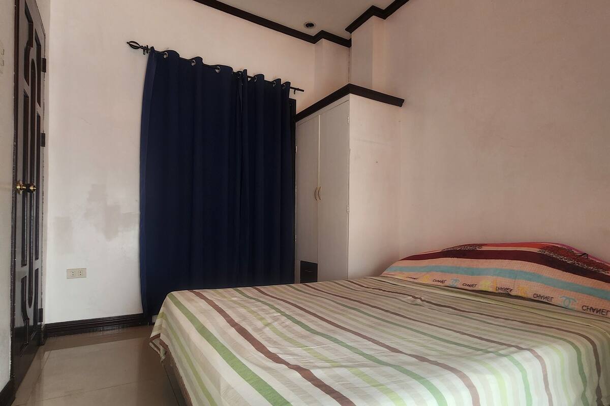 A bedroom with a bed, a window with curtains, a wardrobe, and a tiled floor.