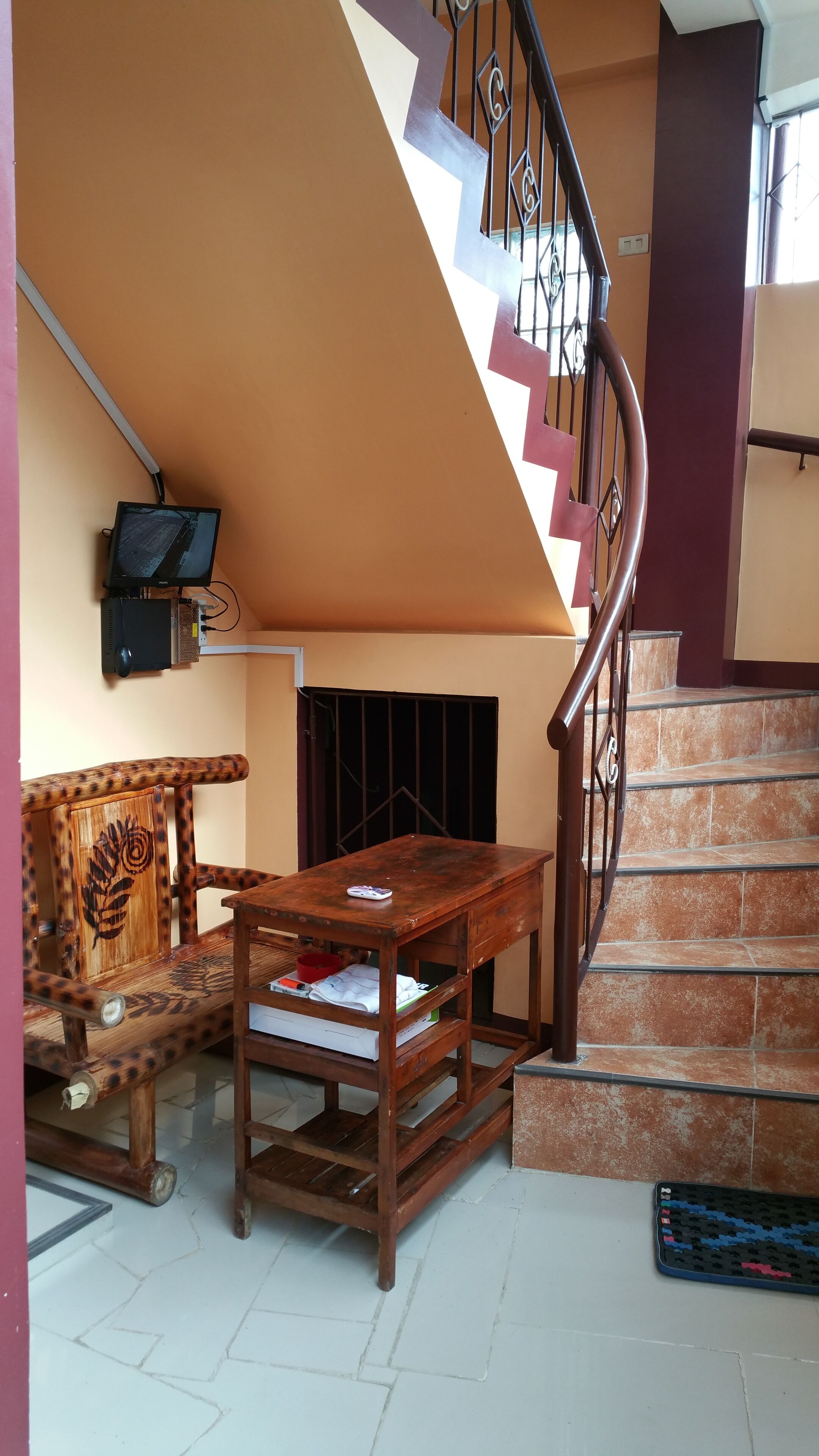 A staircase with a curved railing, a wooden table with papers, a wooden chair, and a television mounted on the wall.