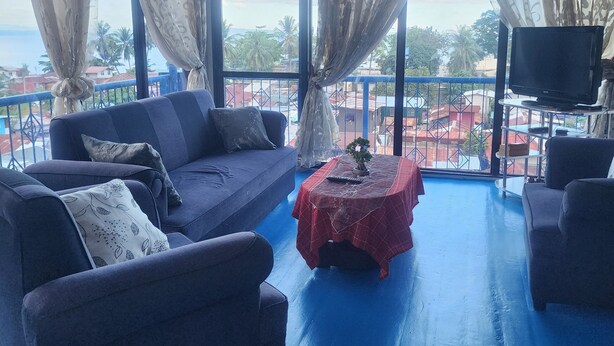 A room with a blue floor, a sofa, a table with a red tablecloth, and a TV on a stand.