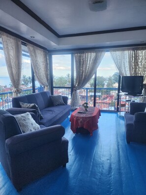 Una habitación con piso azul, un sofá, una mesa con mantel rojo y un televisor sobre un soporte.