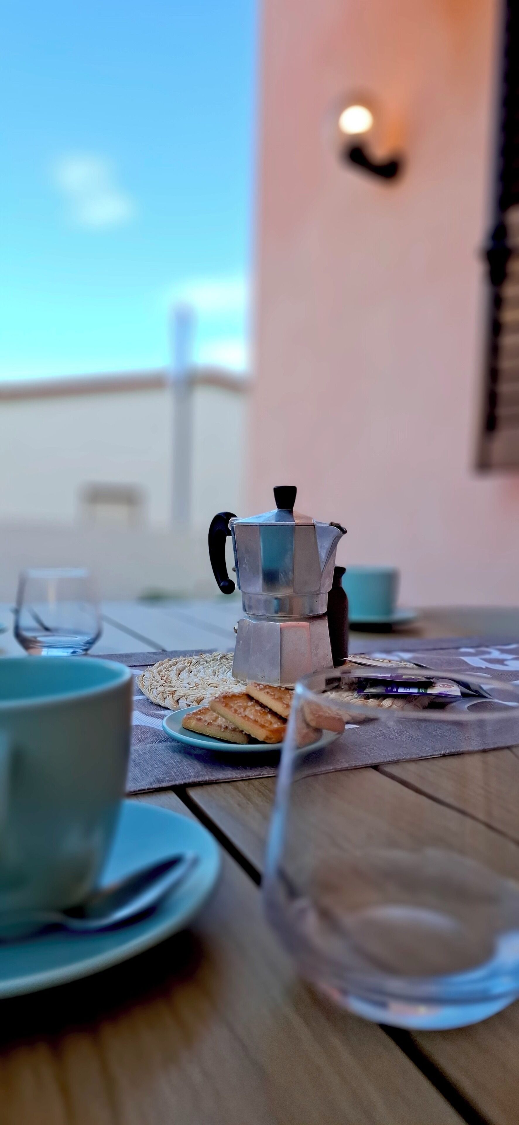 A table with a coffee maker, a plate of cookies, a glass of water, and a cup.
