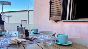 Ein Tisch ist für das Frühstück gedeckt, mit einer Kaffeemaschine, Tassen und Gläsern auf einer Holztischplatte mit einer gewebten Tischmatte.