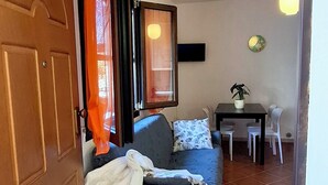 Ein Zimmer mit einem Bett, einem Esstisch mit Stühlen, einer Topfpflanze und einem an der Wand montierten Fernseher.