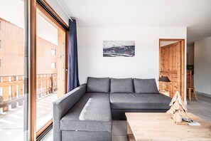 A modern living room with a grey sectional sofa, a wooden coffee table, and a ski lift picture on the wall. - Spacious Apartment at the Foot of the Slopes with Mountain View and Balcony (Morillon)