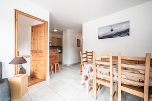 A dining area with a wooden table and chairs, a wooden door, a lamp, and a kitchen in the background. - Spacious Apartment at the Foot of the Slopes with Mountain View and Balcony (Morillon)