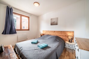 A bedroom with a bed, a wooden headboard, a window with curtains, a bedside table with a lamp, and a radiator. - Spacious Apartment at the Foot of the Slopes with Mountain View and Balcony (Morillon)