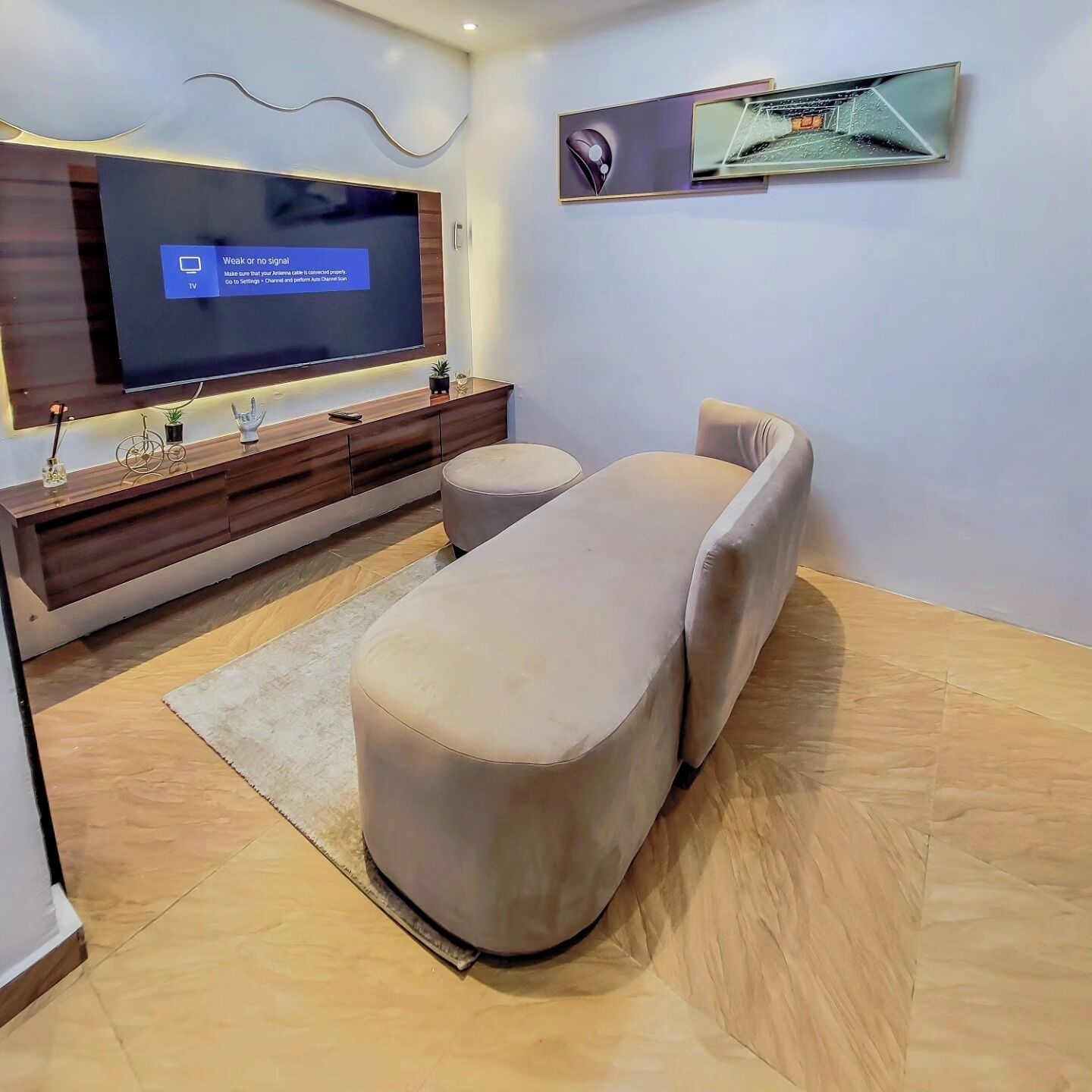 A modern living room with a large flat-screen TV mounted on a wooden wall, a comfortable sofa, and a small ottoman.