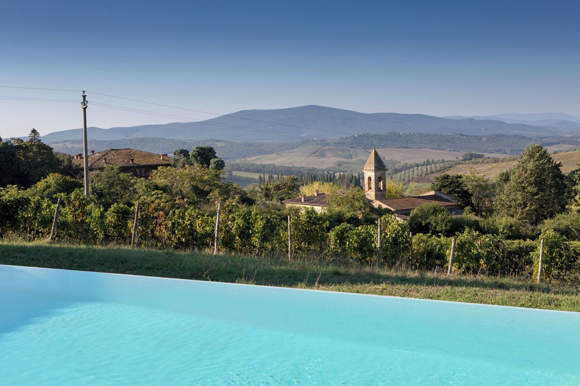 Une piscine avec vue sur les vignes et une église en arrière-plan.