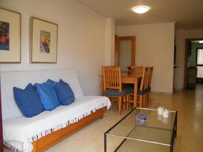 A living room with a sofa, a glass coffee table, and a dining area with wooden chairs and a table. - Family apartment with pool - 6 guests (Gandía)