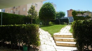 A pathway leading to a building with steps and a garden area with hedges and trees. - Family apartment with pool - 6 guests (Gandía)