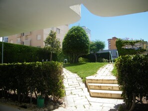 A pathway leading to a building with steps and a garden area with hedges and trees. - Family apartment with pool - 6 guests (Gandía)